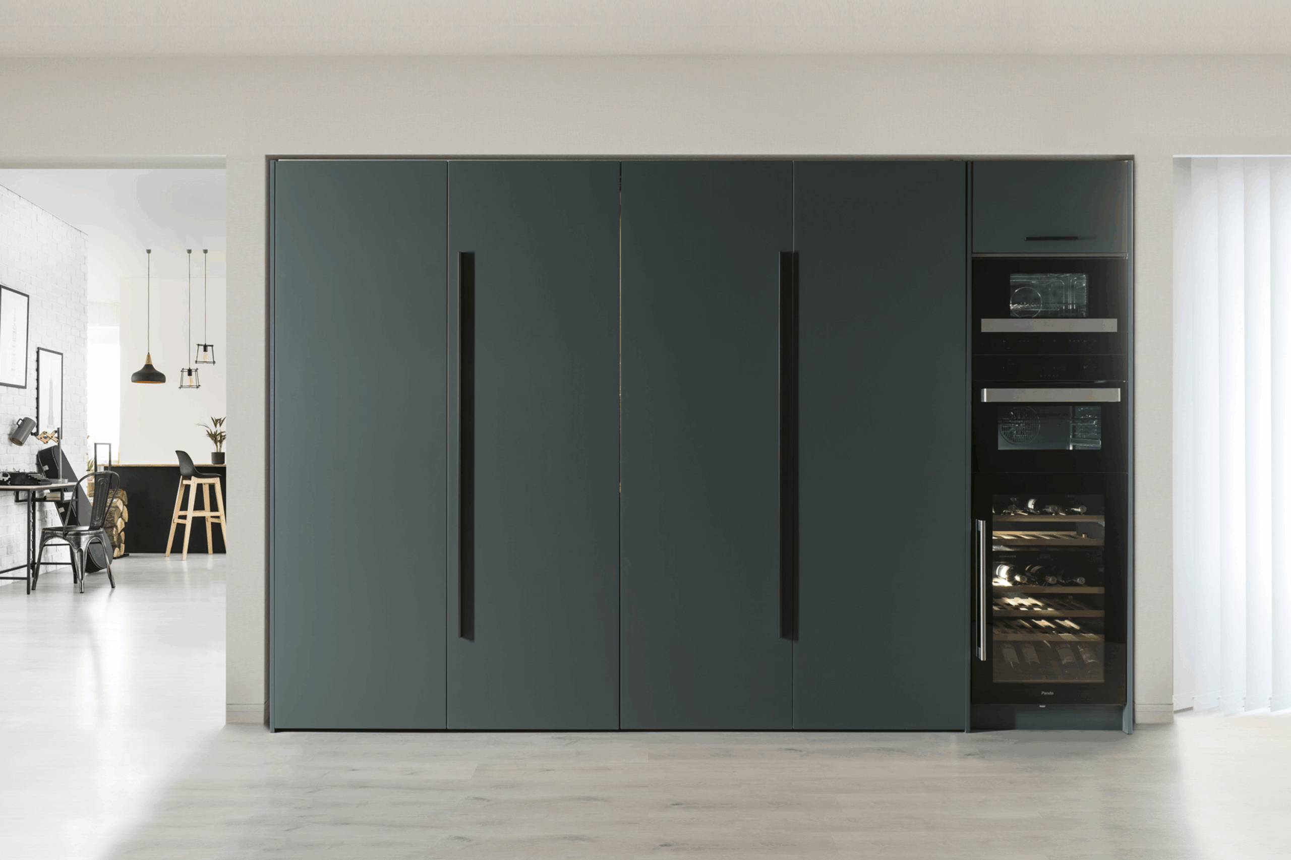 Cocina oculta tras elegantes puertas en gris oscuro con tiradores integrados en negro, que aportan sobriedad y limpieza visual. A la derecha, una columna de electrodomésticos empotrados remata el conjunto con funcionalidad y diseño.